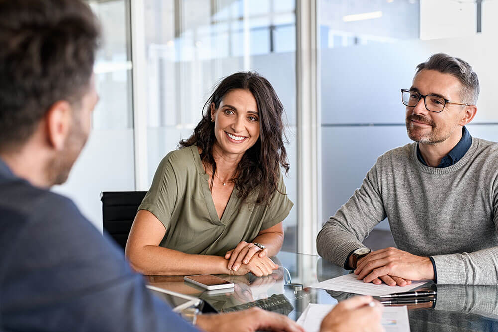Zwei Berater im Gespräch mit einem Paar in einem modernen Büro, alle lächeln freundlich.
